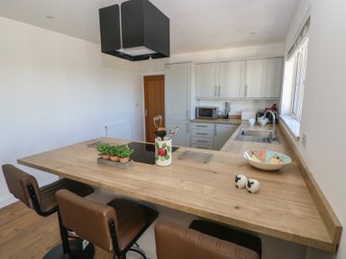 A kitchen with wooden countertops bar stools a sink and cabinets at Arfryn in Solva