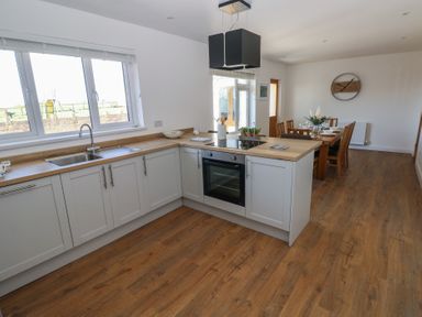 A kitchen with white cabinets and wooden countertops next to a dining area with a wooden table and chairs at Arfryn in Solva