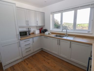 A kitchen with grey cabinets wooden countertop a sink under a window and kitchen appliances at Arfryn in Solva