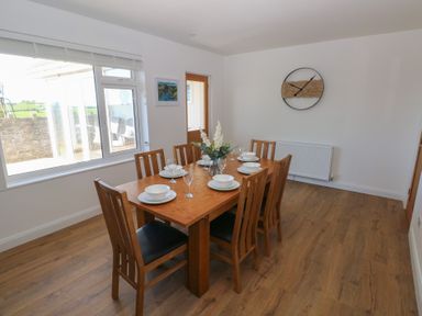 A dining room with a wooden table set for six and a wall clock at Arfryn Solva