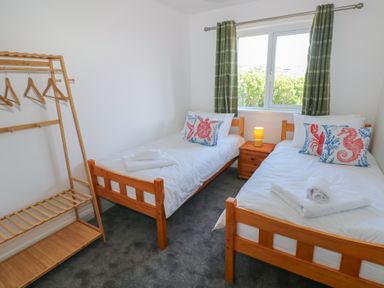 A bedroom with two single beds a wooden clothes rack and a window with green curtains at Arfryn in Solva