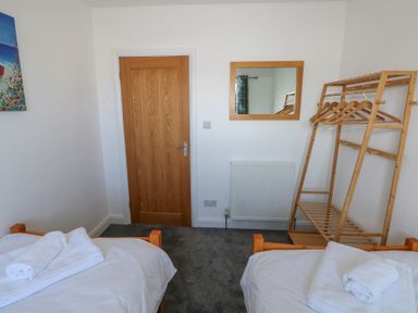 A bedroom with two single beds with white linens a wooden door a wall mirror and a wooden clothes rack with hangers at Arfryn in Solva