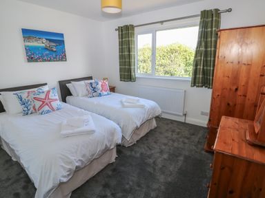 A bedroom with two single beds with white bedding and decorative pillows a wooden wardrobe and chest of drawers a window with green curtains and a painting on the wall at Arfryn in Solva