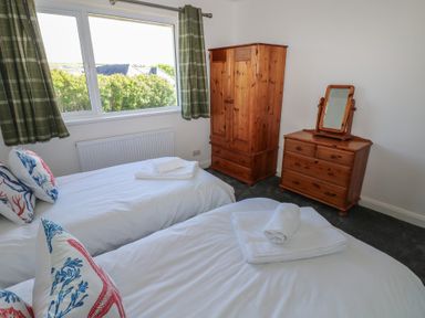 A bedroom with two single beds a wooden wardrobe and a wooden dresser with a mirror at Arfryn Solva