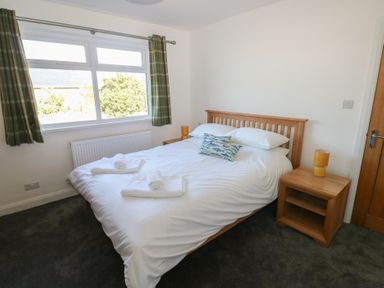 A bedroom with a double bed with white bedding green curtains and wooden bedside tables at Arfryn in Solva