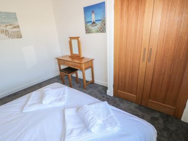 A bedroom with a bed covered in white sheets and towels a wooden dressing table with mirror and stool and a wooden wardrobe at Arfryn in Solva