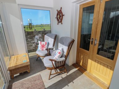 A corner seating area with two armchairs and a wooden chest by glass doors at Arfryn in Solva