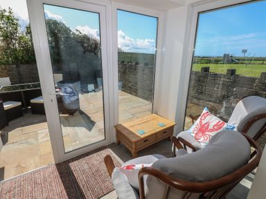 A room with glass doors and windows overlooking a patio with a table and chairs and a grassy area beyond at Arfryn in Solva