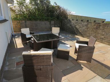 An outdoor patio with wicker chairs and a table surrounded by stone walls at Arfryn in Solva