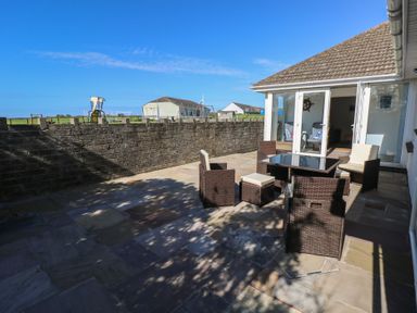 An outdoor patio area with a table and chairs and a low stone wall at Arfryn in Solva