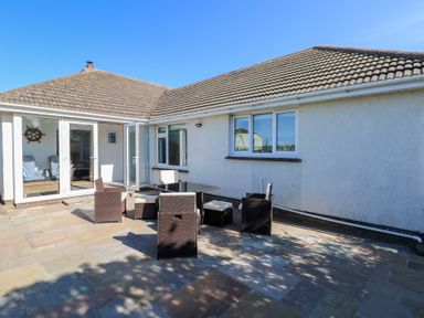 An outdoor patio area with a table and six chairs outside a white house with tiled roof at Arfryn in Solva