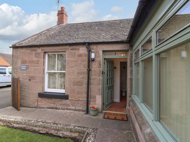 Entrance to a stone cottage with a green door and windows and a tiled roof at Dromore Cottage in Norham