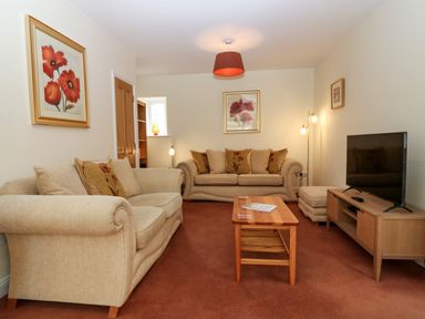 A living room with beige sofas a wooden coffee table a TV on a wooden stand and wall art at Dromore Cottage in Norham