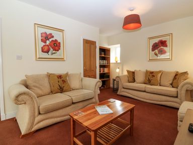 A living room with two beige sofas a wooden coffee table and framed flower pictures on the walls at Dromore Cottage in Norham