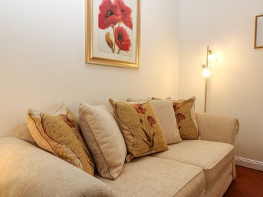 A beige sofa with patterned cushions and a standing lamp in a corner with floral artwork on the wall at Dromore Cottage in Norham