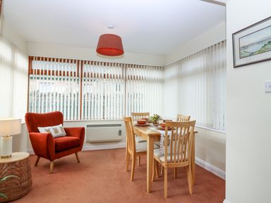 A dining area with a wooden table and chairs and a red armchair next to a window at Dromore Cottage in Norham