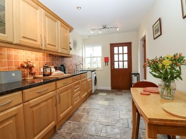 A kitchen with wooden cabinets a table with flowers and a door at Dromore Cottage in Norham