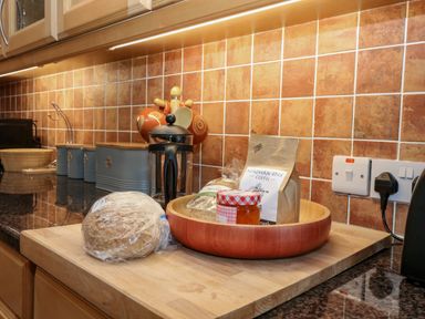 A kitchen counter with a bread loaf plastic wrapped a wooden bowl containing coffee a jar and other items at Dromore Cottage in Norham