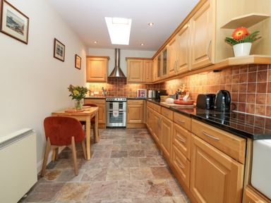A kitchen with wooden cabinets black countertops a stove a dining table with red chairs and flowers at Dromore Cottage in Norham