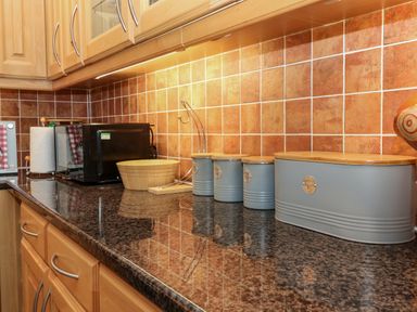 A kitchen counter with a microwave wooden bowl paper towel holder and gray storage canisters at Dromore Cottage in Norham