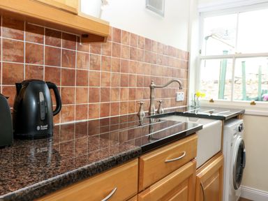 A kitchen counter with a black kettle toaster stovetop sink washing machine under a window at Dromore Cottage in Norham