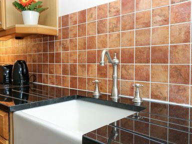 A kitchen sink with silver faucet and black countertop with brown tile backsplash and black appliances at Dromore Cottage in Norham