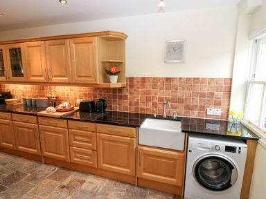 A kitchen with wooden cabinets black countertop a white sink a washing machine and various appliances at Dromore Cottage in Norham