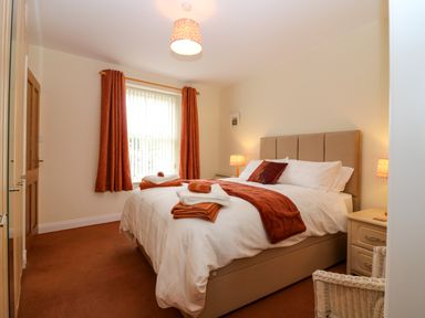 A bedroom with a bed white bedding and orange blankets and towels at Dromore Cottage in Norham
