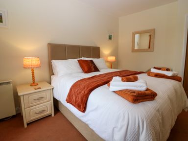 A bedroom with a double bed with white and orange bedding two bedside tables with lamps and folded towels at Dromore Cottage in Norham