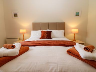 A bedroom with a bed made with white and orange linens and towels on the bed at Dromore Cottage in Norham