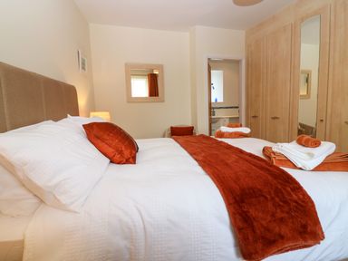 A bedroom with a bed with white linens and rust colored throws next to a wardrobe with mirrored doors at Dromore Cottage in Norham