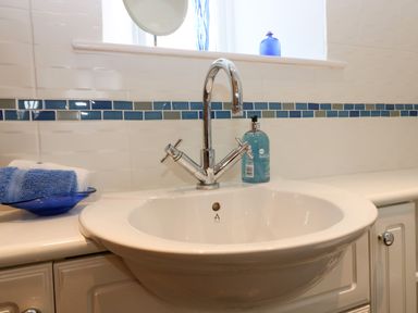 A bathroom sink with a chrome faucet blue and white towels on a dish and a soap dispenser at Dromore Cottage in Norham