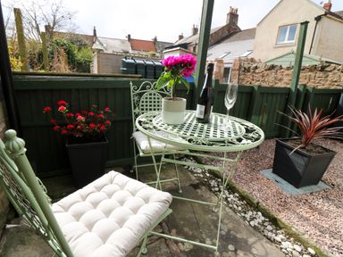 An outdoor patio with a small round table and two chairs with cushions plants on the table and in pots around the area at Dromore Cottage in Norham