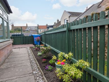 A garden path with flower beds and a green wooden fence at Dromore Cottage in Norham
