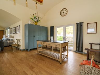 A room with a wooden island table, blue cabinet, chairs, wicker basket, and double glass doors at WildLuing in Cullipool Isle Of Luing