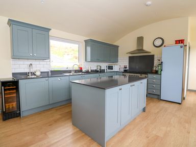 A kitchen with blue cabinets an island a stove a refrigerator and wooden flooring at WildLuing in Cullipool Isle Of Luing