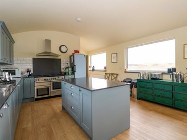 A kitchen with blue cabinets and island a stainless steel stove and hood a green dresser with kitchen appliances and large windows at WildLuing Cullipool Isle Of Luing