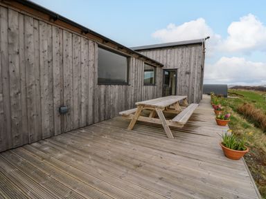 An outdoor wooden deck with a picnic table and potted plants along a wooden building at WildLuing Cullipool Isle Of Luing