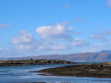 A coastal landscape with rocky shorelines and hills under a blue sky at WildLuing Cullipool Isle Of Luing