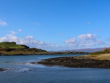 A coastal landscape with water and rocky shoreline under a blue sky at WildLuing in Cullipool Isle Of Luing