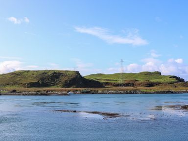 A body of water with an island covered in grass and a metal tower at WildLuing Cullipool Isle Of Luing