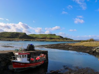 A fishing boat docked by a stone pier in a coastal inlet with grassy hills in the background at WildLuing Cullipool Isle Of Luing