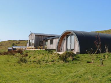 A curved wooden and metal building on a grassy hillside at WildLuing in Cullipool Isle Of Luing
