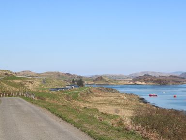 A coastal rural road with grassy hills and small buildings near the water at WildLuing in Cullipool Isle Of Luing