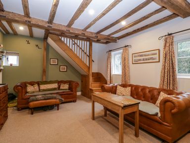 A living room with two leather sofas a wooden table stairs and exposed wooden ceiling beams at 2 Loxter Villas Wellington Heath near Ledbury