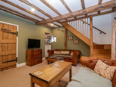 A living room with wooden beams a wooden staircase leather sofas and a wooden cabinet at 2 Loxter Villas Wellington Heath near Ledbury
