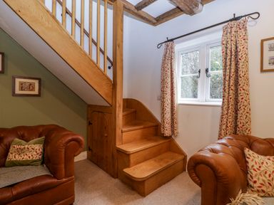 A living area with wooden stairs two leather armchairs and a window with patterned curtains at 2 Loxter Villas Wellington Heath near Ledbury