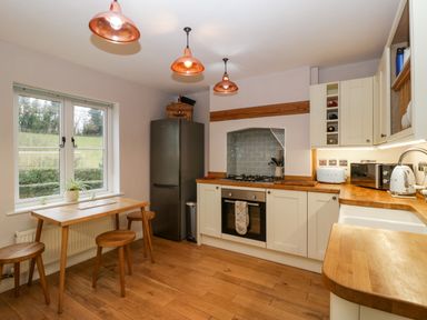 A kitchen with wooden floors white cabinets a wooden table with stools and copper pendant lights at 2 Loxter Villas Wellington Heath near Ledbury