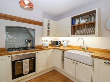 A kitchen with white cabinets wooden countertops a built in oven and stove a double sink and an open shelf with plates and jars at 2 Loxter Villas Wellington Heath near Ledbury