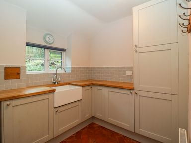 A kitchen with grey cabinets wooden countertops a white sink a window with a clock above it and tiled walls at 2 Loxter Villas Wellington Heath near Ledbury
